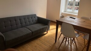 A room with a grey sofa, a wooden dining table, and white chairs. - Holiday Home 'T 2' with Wi-Fi (La Bourboule)