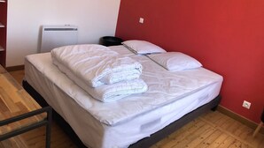 A neatly made bed with white linens, a bedside table, a radiator, and a red wall. - Holiday Home 'T 2' with Wi-Fi (La Bourboule)