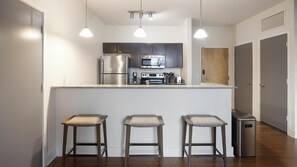 A modern kitchen with stainless steel appliances, a central island with bar stools, and pendant lighting. - Landing | Modern 2BD, Pool, Courtyard (Richmond)