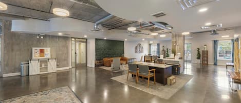 A spacious, modern interior with a central dining area, a reception desk, and a green accent wall.