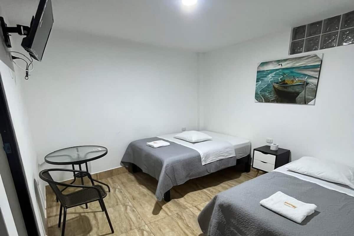 A small, clean room with two beds, a small table, and a TV mounted on the wall.