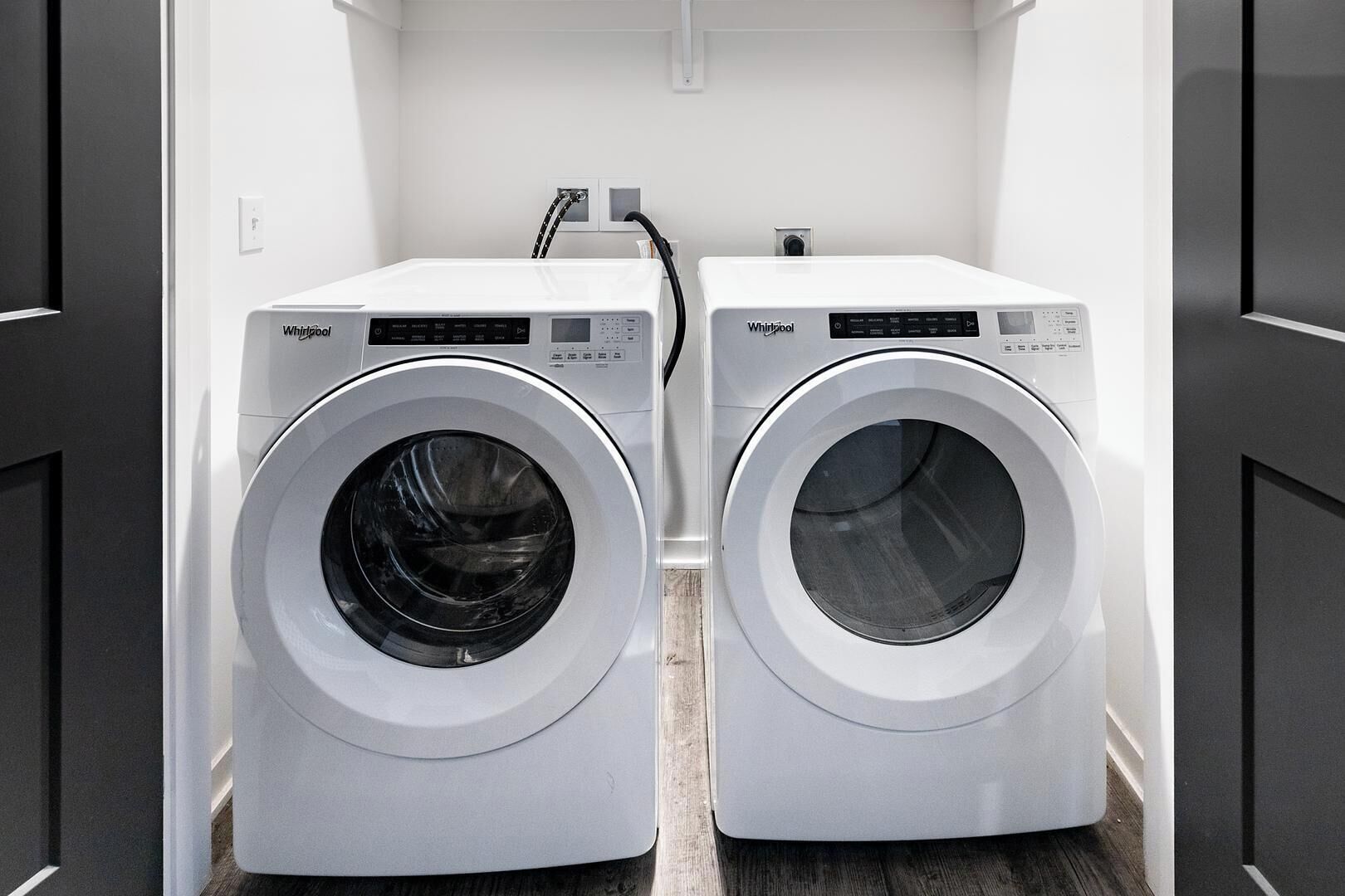 Two Whirlpool front-loading washing machines in a laundry room with a wooden floor and white walls.