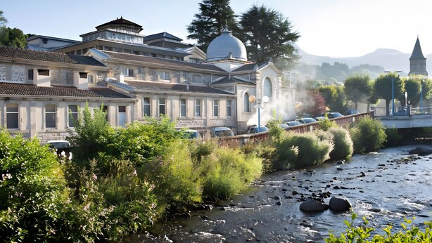 Un edificio histórico con una cúpula destacada, un río en primer plano y un puente al fondo.