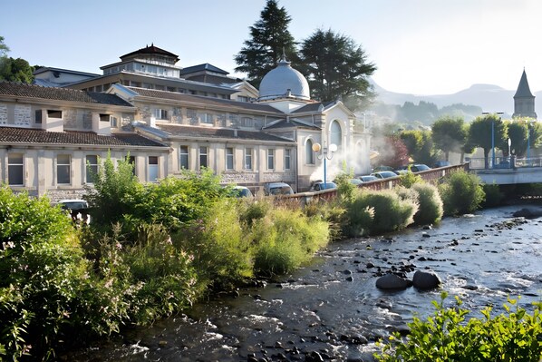 A historic building with a prominent dome, a river in the foreground, and a bridge in the background.