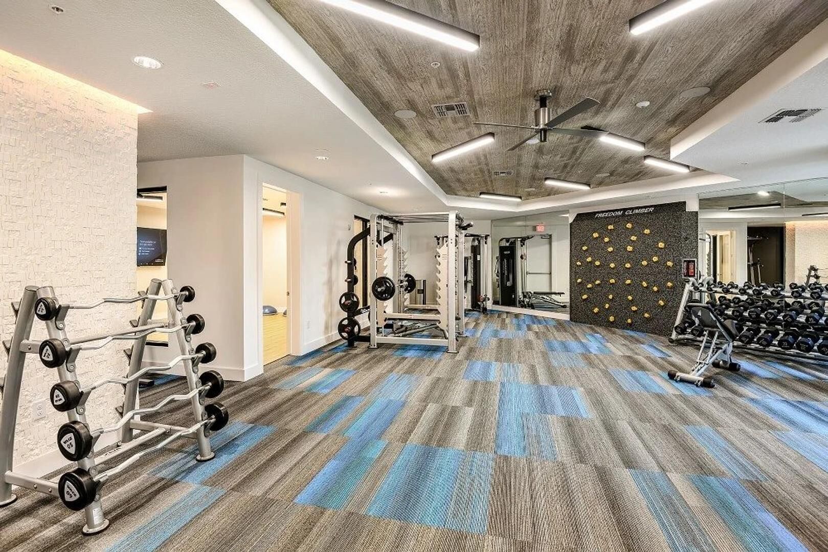 Une salle de sport équipée de matériel de musculation, d’un mur d’escalade et d’un ventilateur au plafond.