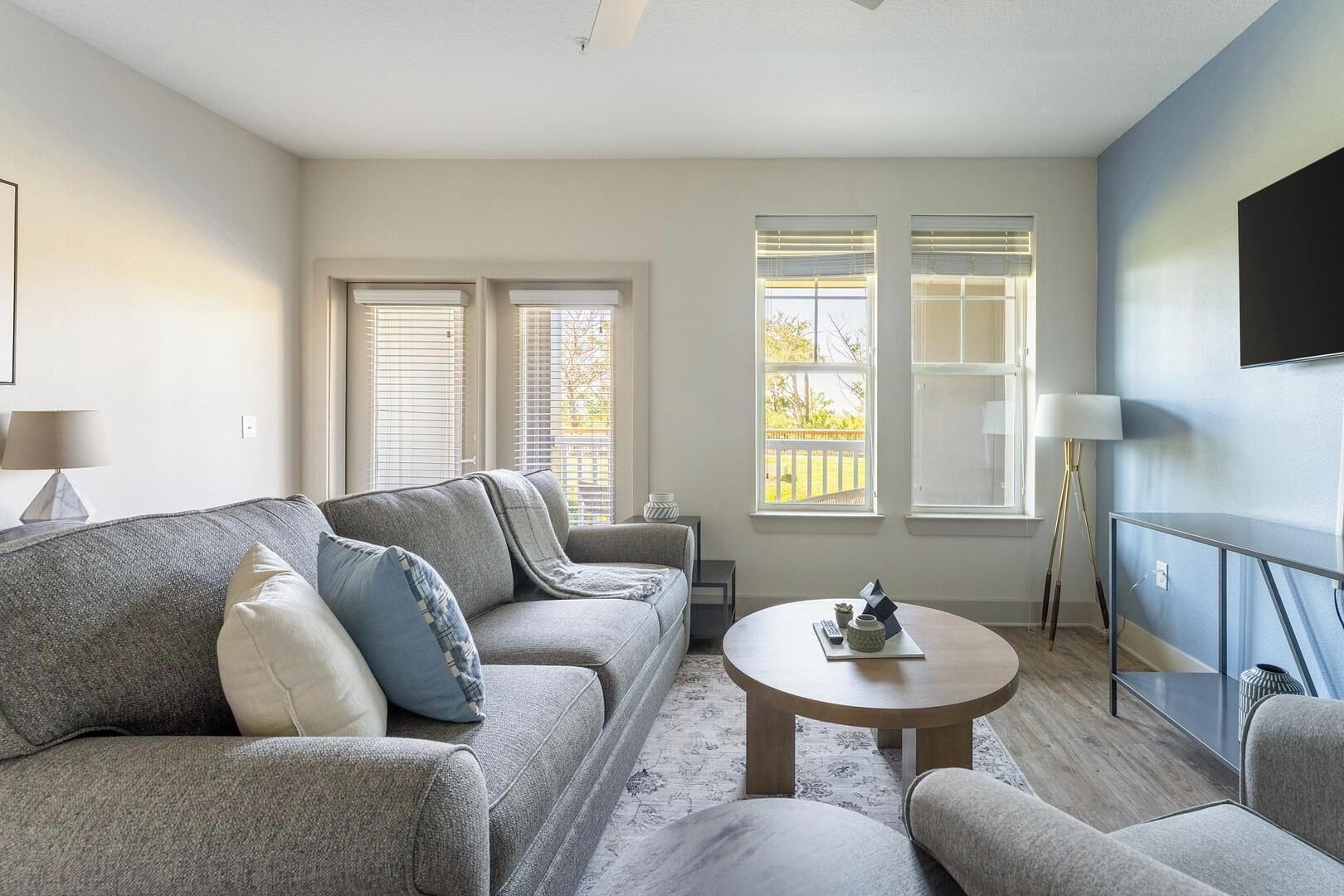 A modern living room with a grey sofa set, a round coffee table, and a TV mounted on a blue wall.