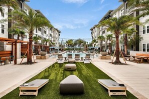 A pool area with lounge chairs and a central water feature, surrounded by palm trees and a grassy lawn. - Landing | Beautiful 1BD, Pool, Yoga Studio (St. Augustine)