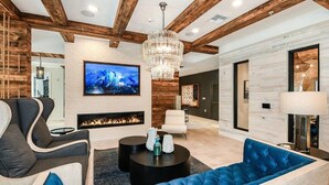 A modern living room with exposed wooden beams, a fireplace, a large TV, and a blue sofa. - Landing | Beautiful 1BD, Pool, Yoga Studio (St. Augustine)