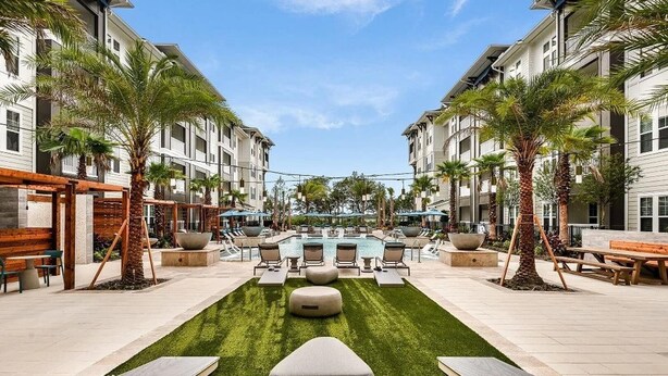 A pool area with lounge chairs and a central water feature, surrounded by palm trees and a grassy lawn. - Landing | Spectacular 2BD, Yoga Studio, Pool (St. Augustine)