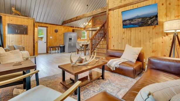 L’intérieur chaleureux d’un chalet, avec un revêtement mural en bois, un coin repas, une cuisine et un salon doté de canapés en cuir et d’une cheminée.