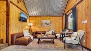 Un salon chaleureux avec des murs en bois, un canapé en cuir marron, une table basse et un téléviseur fixé au mur.