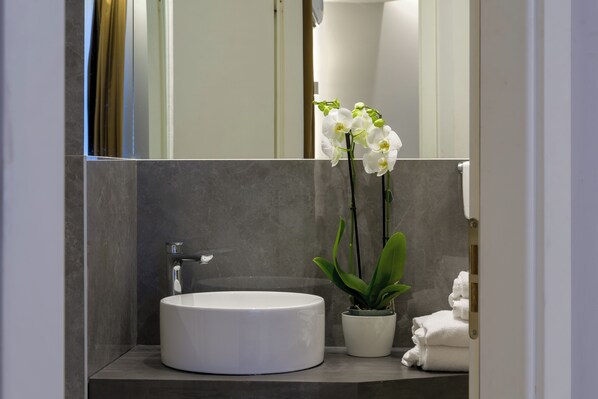Een moderne badkamer met een ronde witte wasbak, een potplant en een stapel witte handdoeken.