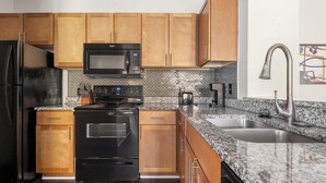 A kitchen with wooden cabinets, a black stove, a microwave, a coffee maker, and a stainless steel sink. - Landing | Spectacular 2BD, Tennis Court, Gym (Gainesville)