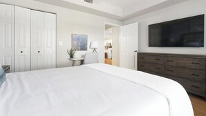 Een slaapkamer met een groot bed, een dressoir, een televisie en een deur naar een badkamer.