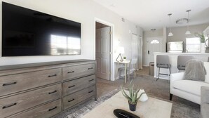 Een moderne woonkamer met een flatscreen televisie, een houten kast en een eethoek met stoelen en een tafel.