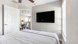 Un dormitorio con una cama, un televisor montado en la pared y una puerta que da al baño.