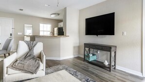 Una sala de estar con televisor, sofá, mesa de centro y una cocina al fondo.