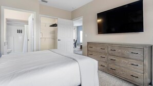 A bedroom with a large bed, a wooden dresser, a TV on the wall, and a walk-in closet. - Landing | Chic 2BD, Gym, Clubhouse (North Port)