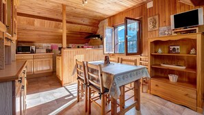 Interior de uma cabana de madeira com mesa de jantar, cadeiras, cozinha e televisão.