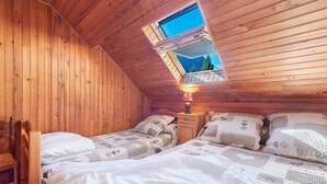Um quarto aconchegante com paredes de madeira, duas camas com roupa de cama estampada, uma mesa de cabeceira com abajur e um claraboia.