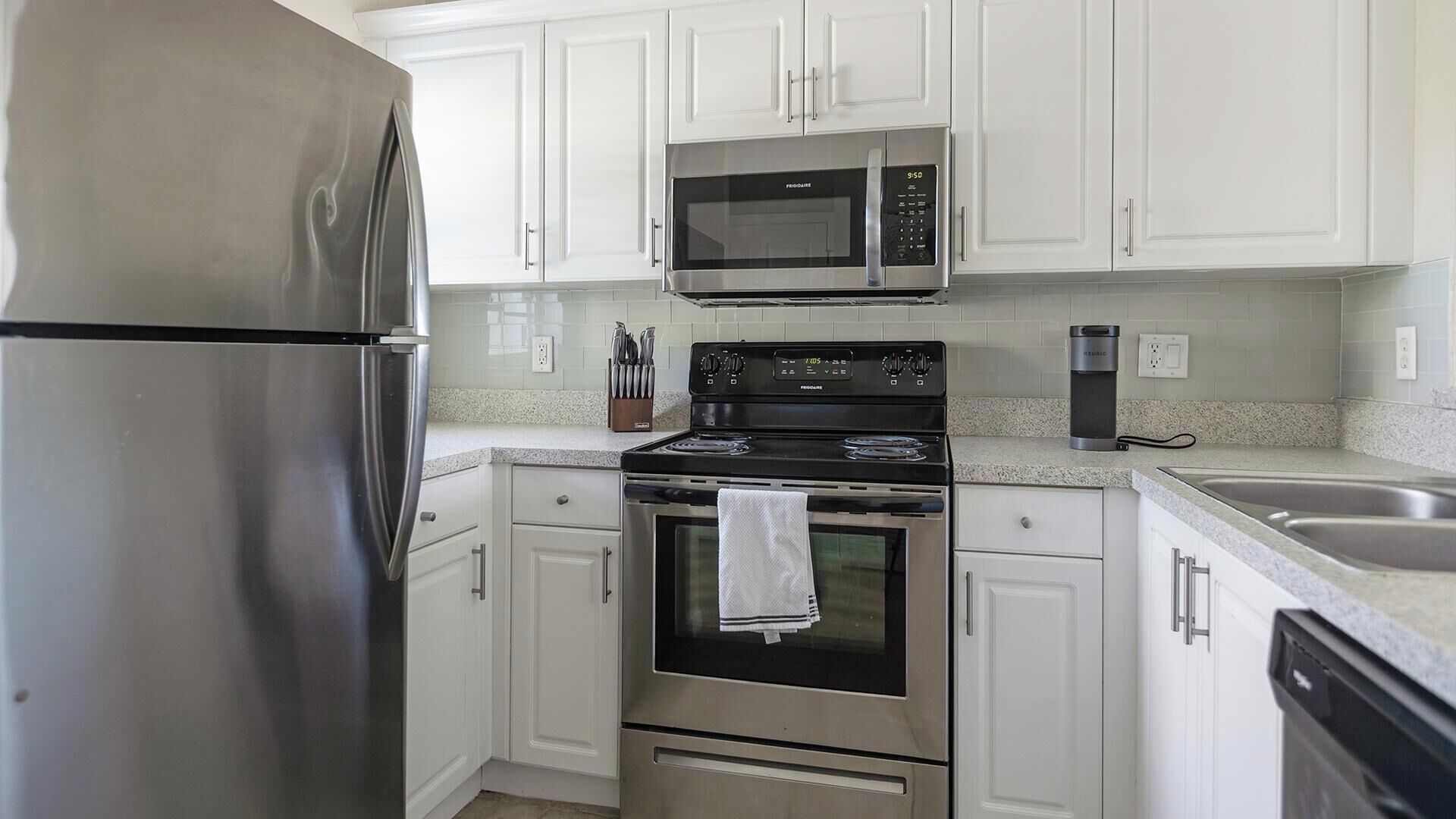 A kitchen with stainless steel appliances, white cabinetry, and a granite countertop.