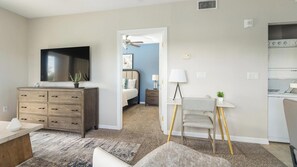 A bedroom with a bed, a dresser, a TV, and a desk with a chair.