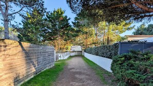 En grusgång som kantas av trästaket och tät buskvegetation, och som leder fram till en byggnad med ett sluttande tak.