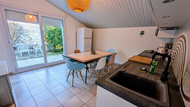 Ett modernt kök med en stor diskho, en matplats med bord och stolar samt en skjutdörr i glas som leder ut till en uteplats.