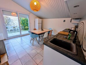 A modern kitchen with a large sink, a dining area with a table and chairs, and a sliding glass door leading to an outdoor patio. - Pretty house in a quiet area 100m from the beach (La Tranche-sur-Mer)