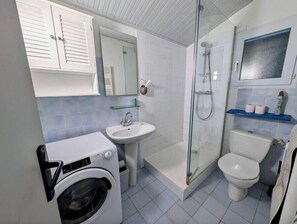 Kompakti kylpyhuone, jossa on pesukone, pesuallas, wc ja lasinen suihkuseinä.
