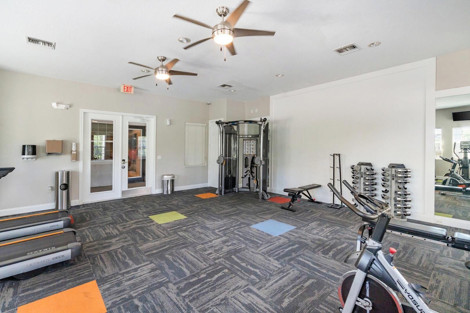 A gym with treadmills, a weight bench, a squat rack, and a ceiling fan.