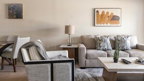 A modern living room with a sofa, armchair, and coffee table. There is a lamp on a side table and a framed artwork on the wall. - Landing | Modern 1BD, Courtyard, Gym (North Port)