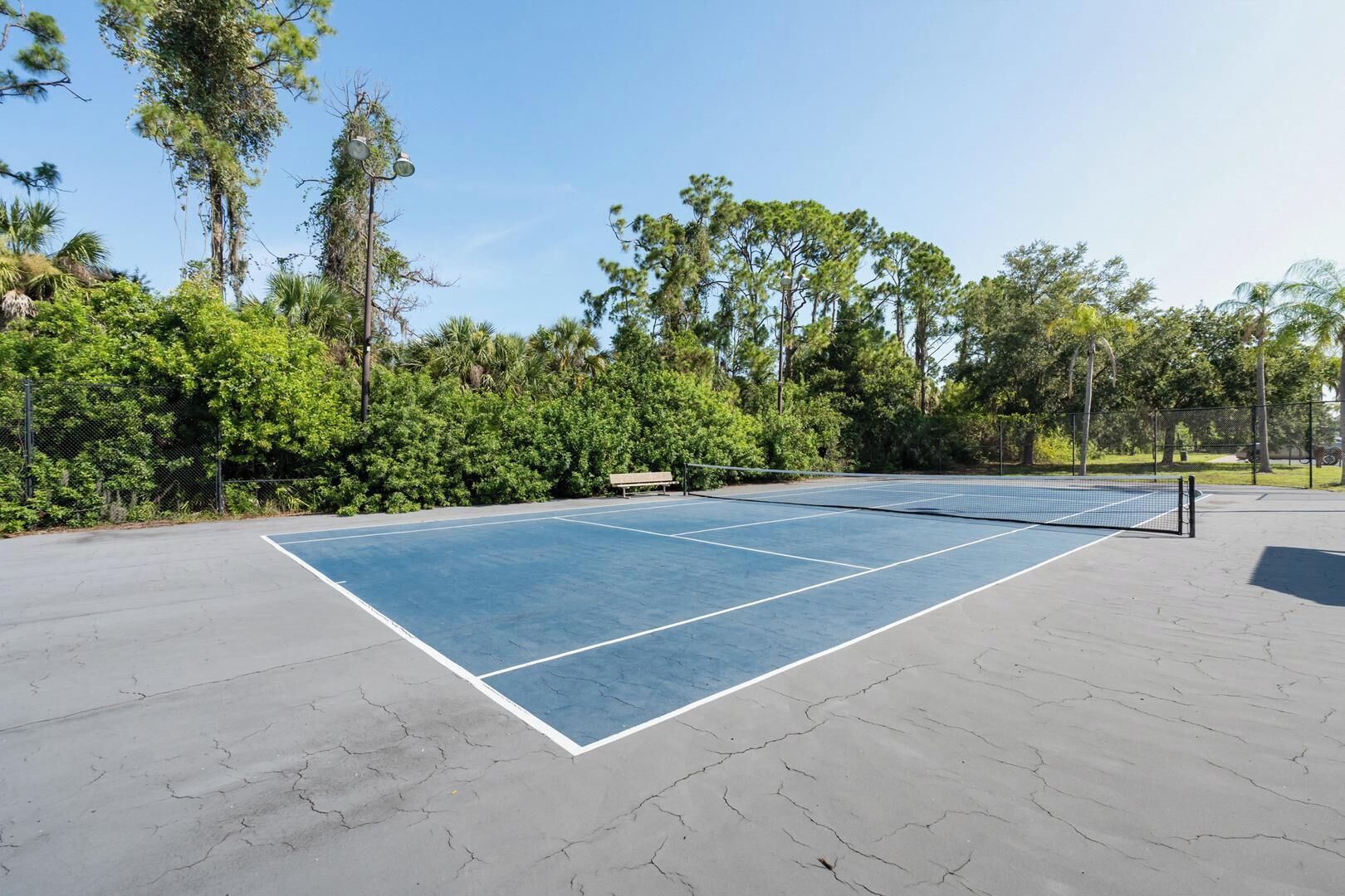An outdoor tennis court with a net, surrounded by trees and a fence.