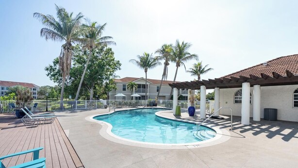 A swimming pool with a wooden deck, lounge chairs, and palm trees. - Landing | Modern 1BD, Clubhouse, Gym (North Port)