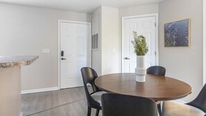 A dining area with a round table, two chairs, a vase with flowers, and a framed picture on the wall.