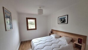 A bedroom with a wooden bed, a nightstand, a wall-mounted lamp, and two framed pictures. - Modern apartment in the heart of Séez (Séez)