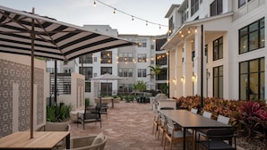 An outdoor patio area with tables and chairs, string lights, and a patterned wall. - Landing | Beautiful 2BD, Game Room, Pool (Longboat Key)
