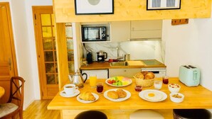 Une table en bois dressée pour le petit-déjeuner, avec des assiettes de croissants, des fruits et du café.