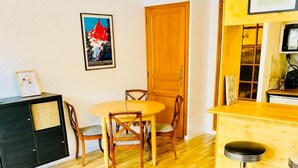 Un coin repas avec une table ronde et des chaises, un petit bar avec des tabourets et un canapé agrémenté d’un coussin rouge.