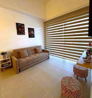 Ein Wohnzimmer mit einem beigen Sofa, einem kleinen Beistelltisch mit einer Pflanze und einem gemusterten Hocker.