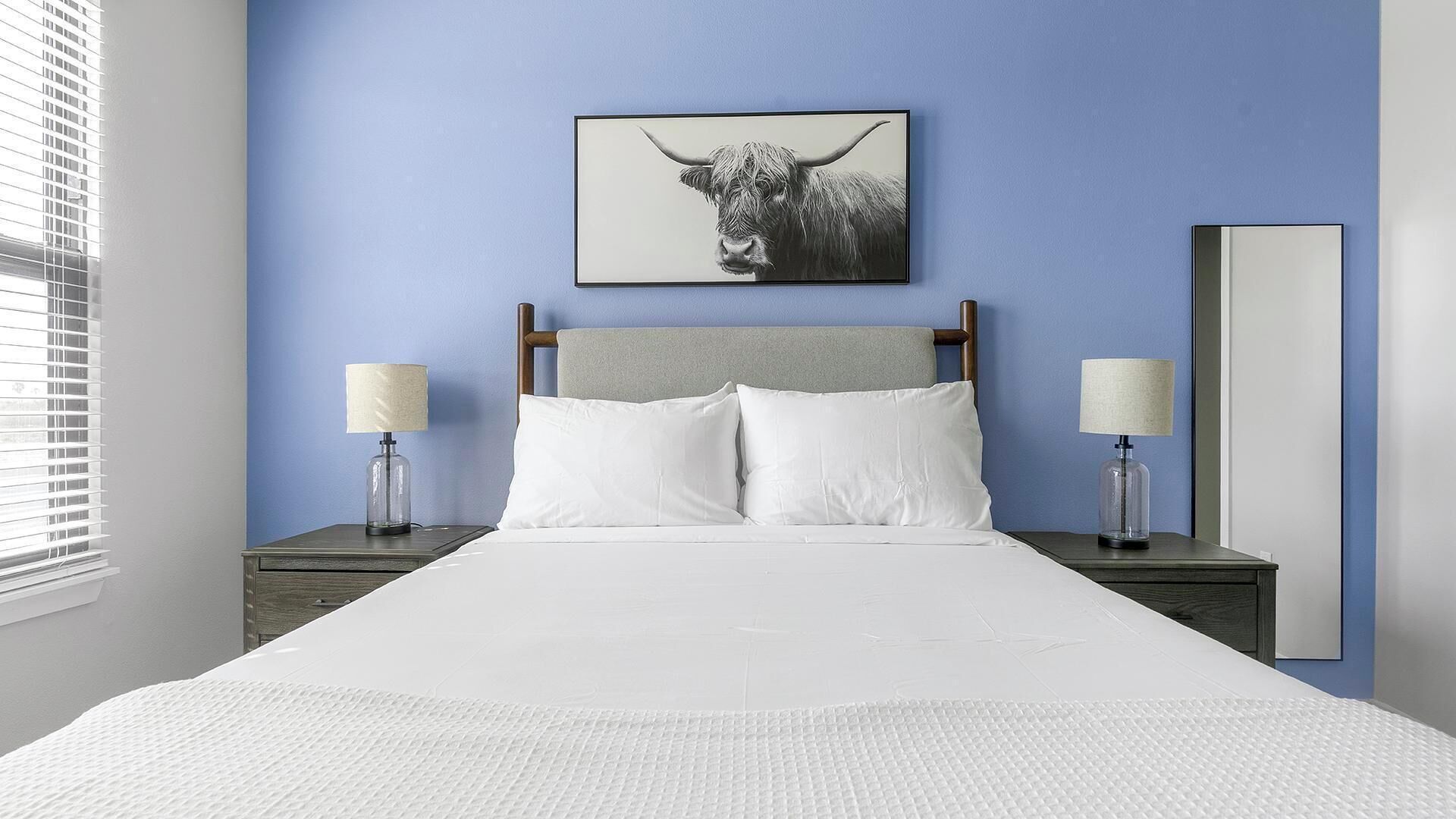 Ein Schlafzimmer mit einem Bett, zwei Nachttischen, einem Wandspiegel und einem Bilderrahmen mit einem Stierbild.