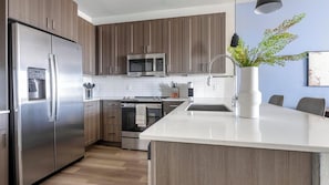 Eine moderne Küche mit Holzschränken, Edelstahlgeräten und einer weißen Arbeitsplatte.