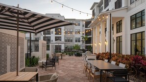 An outdoor patio area with tables and chairs, string lights, and a patterned wall. - Landing | Amazing 1BD, Gym, Game Room (Longboat Key)