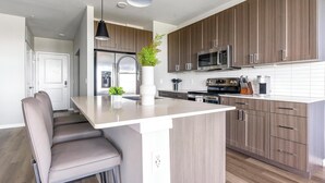 A modern kitchen with a central island, stainless steel appliances, and light wood cabinetry. - Landing | Amazing 1BD, Gym, Game Room (Longboat Key)