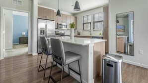 A modern kitchen with a central island, stainless steel appliances, and a view to the dining area. - Landing | Chic 2BD, Game Room, Pool (Longboat Key)