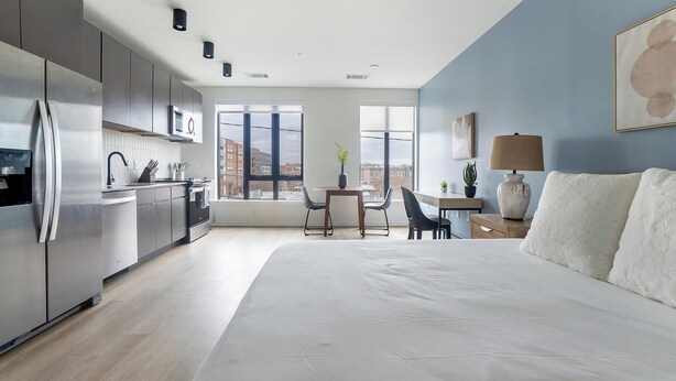 Quarto de hotel moderno com uma cama grande, uma cozinha e uma mesa de jantar com cadeiras.