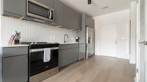 A modern kitchen with grey cabinetry, a stainless steel microwave, a built-in oven, and a refrigerator. - Landing | Modern 1BD, Rooftop Lounge, Pool (Durham)