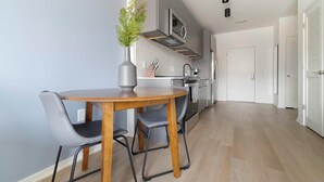 A modern kitchen with a dining area, including a wooden table and chairs, a vase with greenery, and a built-in oven. - Landing | Modern 1BD, Rooftop Lounge, Pool (Durham)