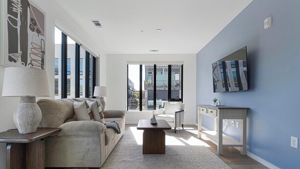 A modern living room with a sofa, coffee table, and a TV mounted on the wall. - Landing | Amazing 2BD, Pool, Rooftop Lounge (Durham)