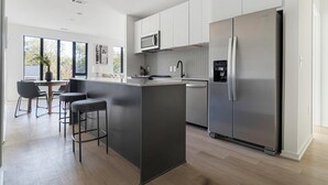 A modern kitchen with a central island, stainless steel appliances, and a dining area with bar stools. - Landing | Amazing 2BD, Pool, Rooftop Lounge (Durham)